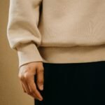 A detailed view of a person wearing a beige sweatshirt and black pants in a relaxed setting.